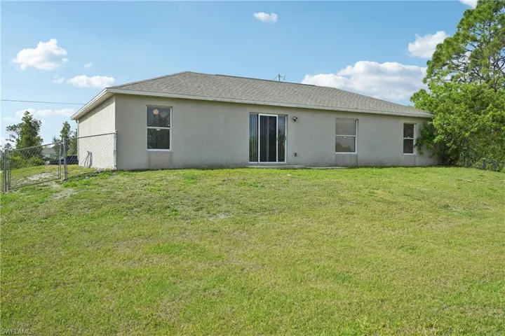 Back of house with stucco siding, fence, and a yard