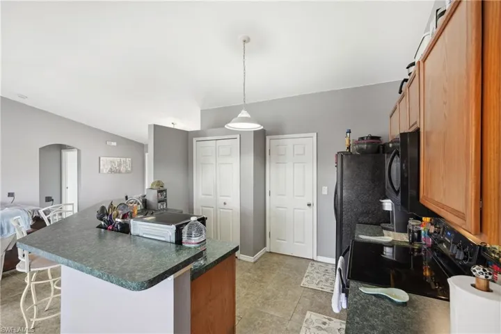Kitchen featuring vaulted ceiling, a kitchen island, dark countertops, black appliances, and arched walkways