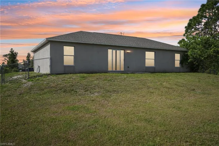 Rear view of property with stucco siding, fence, and a yard