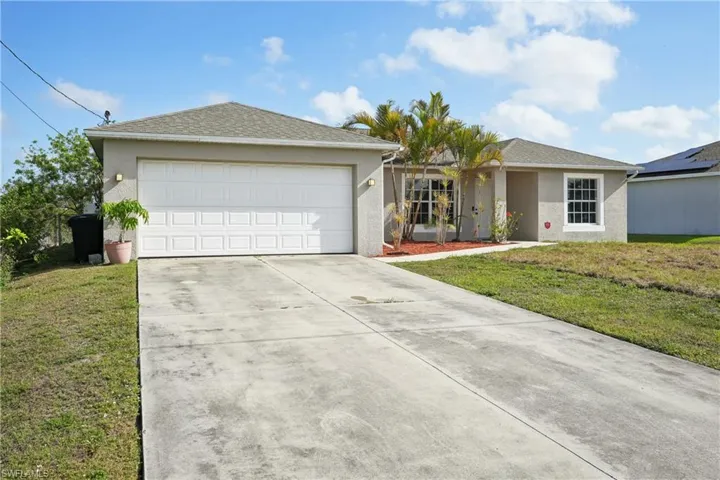 Ranch-style home with a garage, concrete driveway, a front lawn, stucco siding, and a shingled roof
