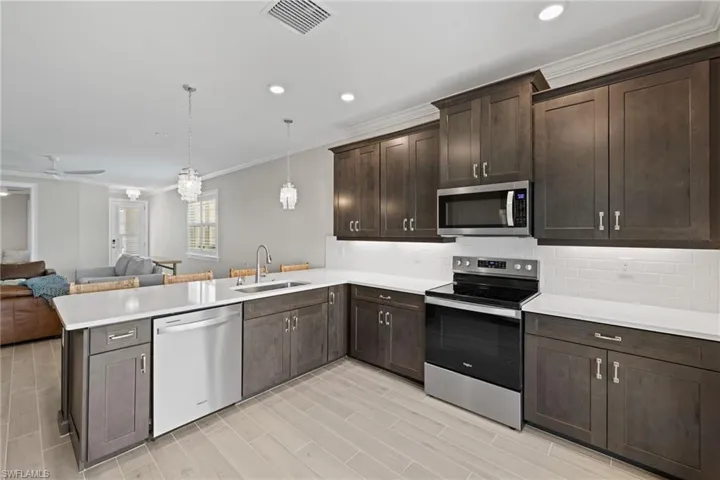 Kitchen with kitchen peninsula, appliances with stainless steel finishes, decorative backsplash, dark brown cabinetry, and sink