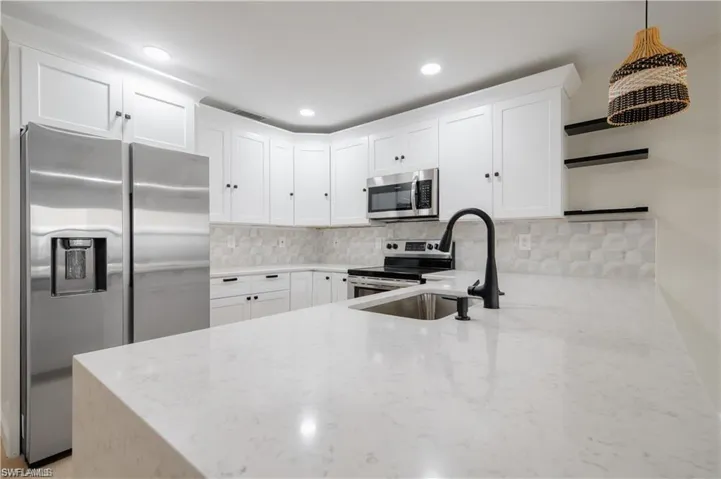 Kitchen featuring stainless steel appliances, light stone counters, tasteful backsplash, white cabinets, and a peninsula