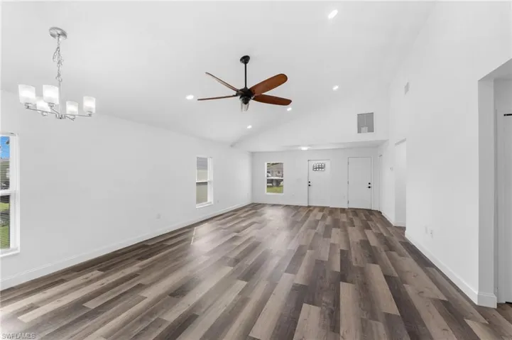 Unfurnished living room with high vaulted ceiling, dark wood-type flooring, recessed lighting, ceiling fan, and a chandelier
