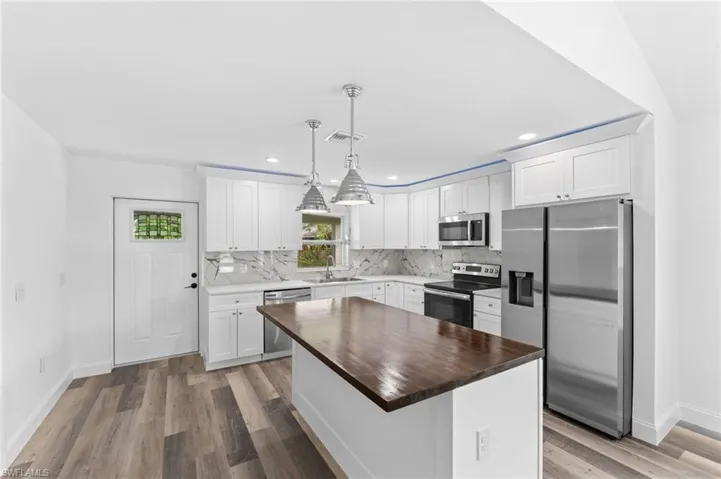 Kitchen featuring wood counters, stainless steel appliances, white cabinets, decorative light fixtures, and light wood-style floors
