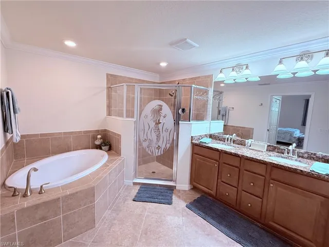 Bathroom featuring an oval soaking tub with tile surround, a glass-enclosed shower with custom etched detailing, a dual-sink vanity with stone-surfaced countertop, and recessed lighting
