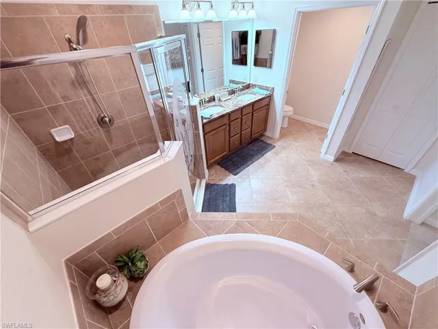 Bathroom featuring a jetted soaking tub, tiled walk-in shower with glass enclosure, dual-sink vanity with stone-surfaced countertop, and tile flooring