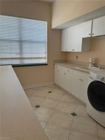 Laundry room with washer / clothes dryer, sink, light tile patterned floors, and cabinets