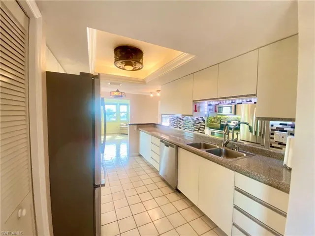 Kitchen featuring light sink, a tray ceiling, appliances with stainless steel finishes, and white cabinets