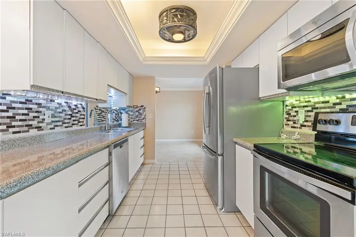 Kitchen with a raised ceiling, sink, tasteful backsplash, white cabinetry, and appliances with stainless steel finishes