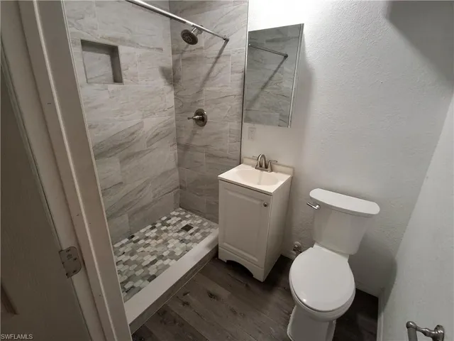 Bathroom featuring a walk-in shower with large format wall tiles and mosaic floor tiles, a built-in shower niche, a single vanity with storage, and wood-finish flooring