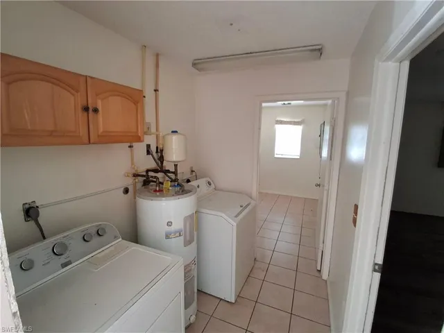 Dedicated utility area featuring white tiled flooring, overhead wood-finish cabinetry, and a water heater