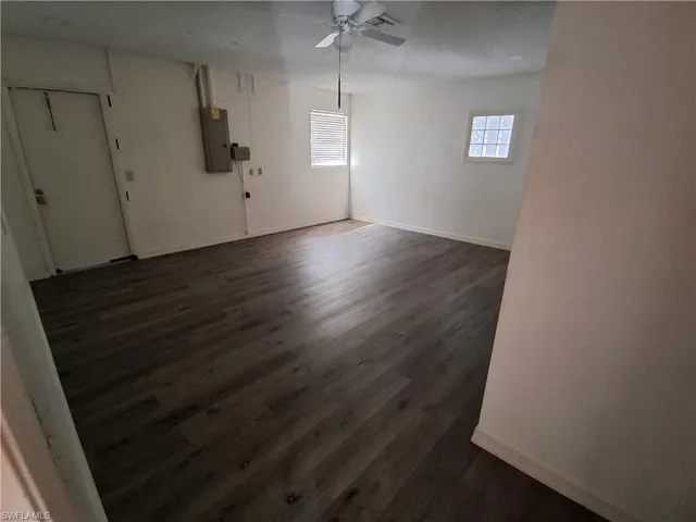 Spacious room featuring wood-finish flooring, white walls, and a ceiling fan