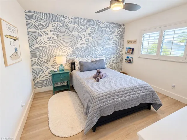 Room featuring wood-finish flooring, a decorative accent wall, a ceiling fan with integrated lighting, and plantation shutters
