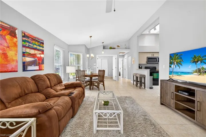 Living room featuring a ceiling fan, light tile patterned flooring, vaulted ceiling, and a chandelier