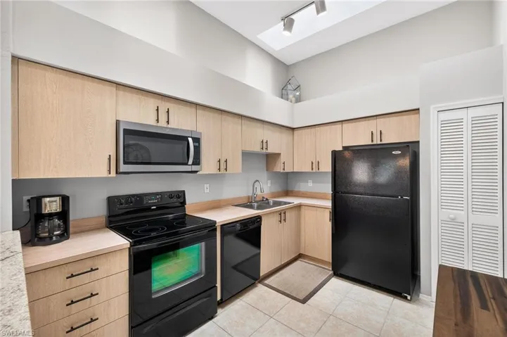 Kitchen featuring black appliances, light countertops, a skylight, light wood finish cabinetry, and track lighting