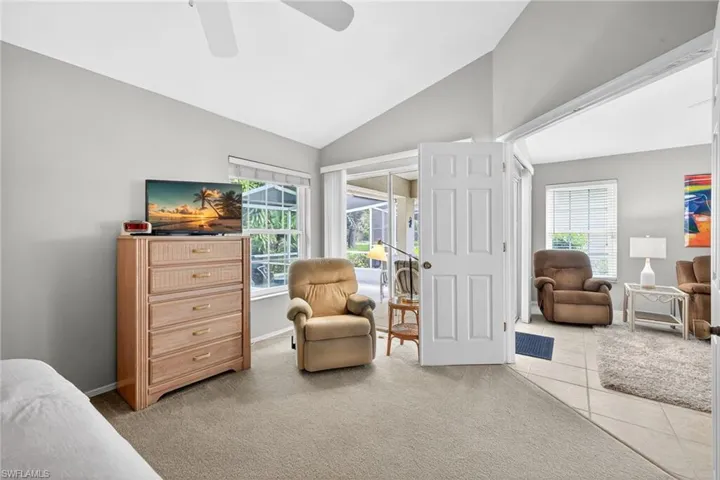 Living area with light colored carpet, vaulted ceiling, a ceiling fan, plenty of natural light, and light tile patterned floors