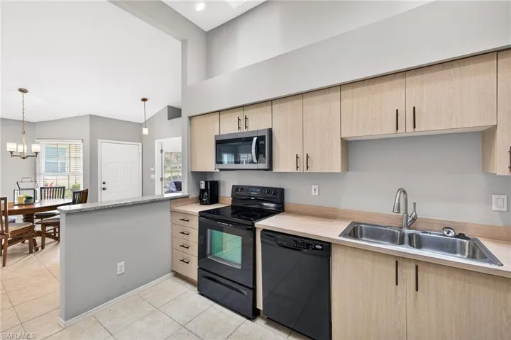 Kitchen with black appliances, light wood finish cabinets, a peninsula, a high ceiling, and hanging lights