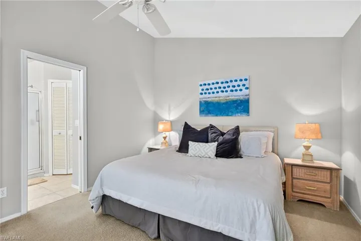 Bedroom featuring light colored carpet, lofted ceiling, ceiling fan, and ensuite bath