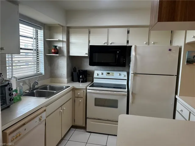 Kitchen featuring white cabinetry, solid-surface countertops, dual-basin stainless steel sink, tile flooring, and built-in appliances