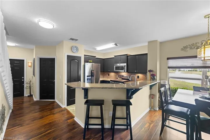 Kitchen with a kitchen bar, appliances with stainless steel finishes, kitchen peninsula, dark wood-type flooring, and backsplash