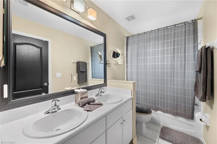 Full bathroom with vanity, toilet, shower / bathtub combination with curtain, and tile patterned flooring