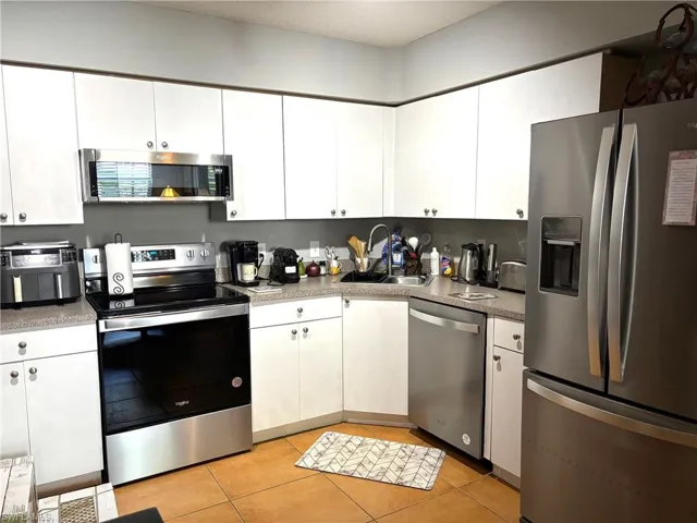 Kitchen with stainless steel appliances, light tile patterned flooring, white cabinetry, a textured ceiling, and light countertops