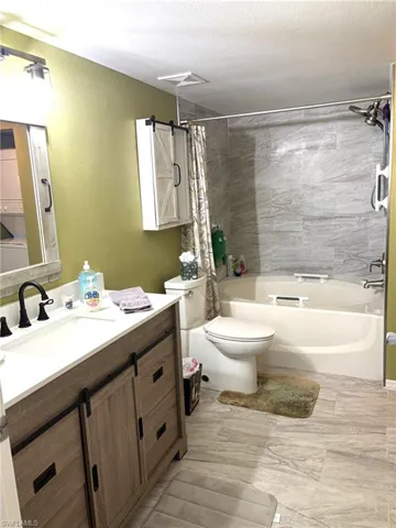 Bathroom with vanity, shower / bath combo with shower curtain, a textured wall, a textured ceiling, and stacked washer / drying machine