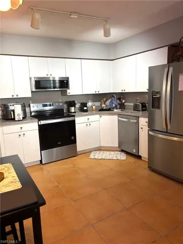 Kitchen with stainless steel appliances, white cabinetry, rail lighting, light tile patterned floors, and light countertops