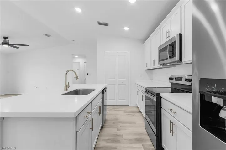 Kitchen featuring an island with sink, sink, vaulted ceiling, light hardwood / wood-style floors, and appliances with stainless steel finishes