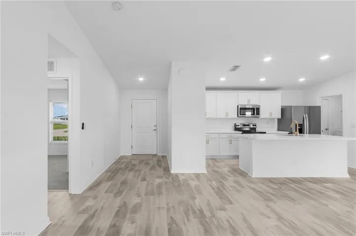 Kitchen featuring appliances with stainless steel finishes, white cabinets, sink, light hardwood / wood-style floors, and a kitchen island with sink