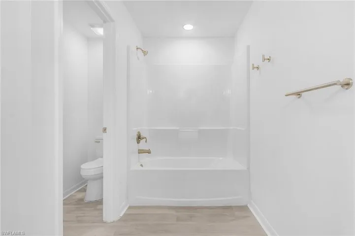 Bathroom featuring shower / washtub combination, hardwood / wood-style flooring, and toilet