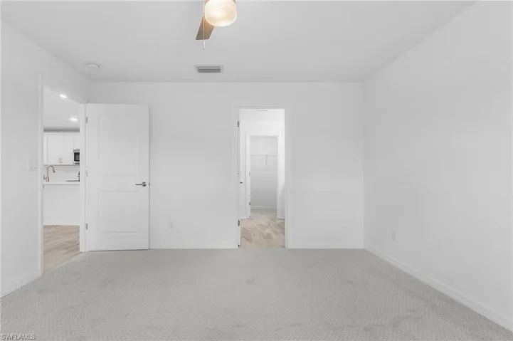 Unfurnished bedroom featuring a spacious closet, light carpet, ceiling fan, and a closet