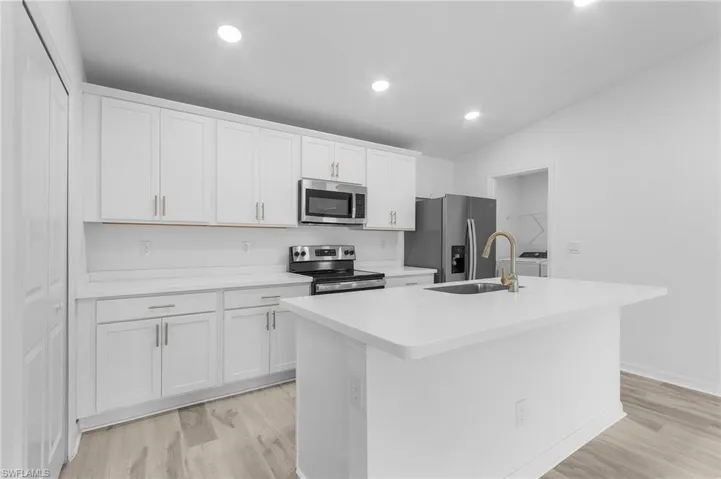Kitchen featuring appliances with stainless steel finishes, light hardwood / wood-style floors, and an island with sink
