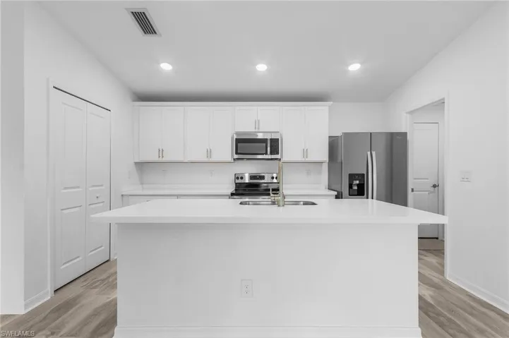 Kitchen featuring white cabinetry, stainless steel appliances, light hardwood / wood-style floors, and a kitchen island with sink