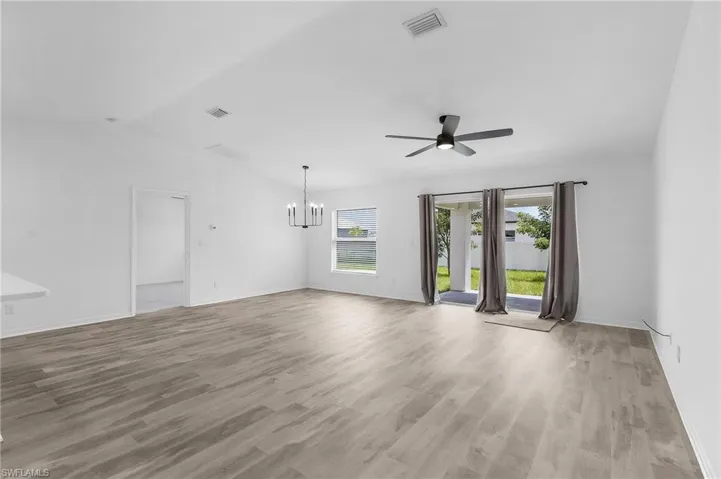 Spare room featuring ceiling fan with notable chandelier, lofted ceiling, and light hardwood / wood-style floors