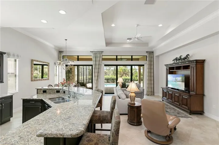 Kitchen with a kitchen island with sink, a breakfast bar area, a raised ceiling, light stone counters, and a ceiling fan