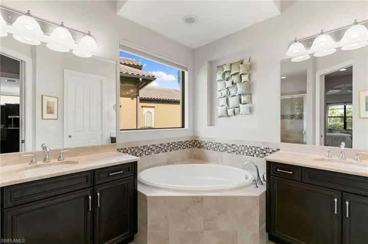 Full bath featuring ensuite bath, two vanities, a garden tub, and a shower stall