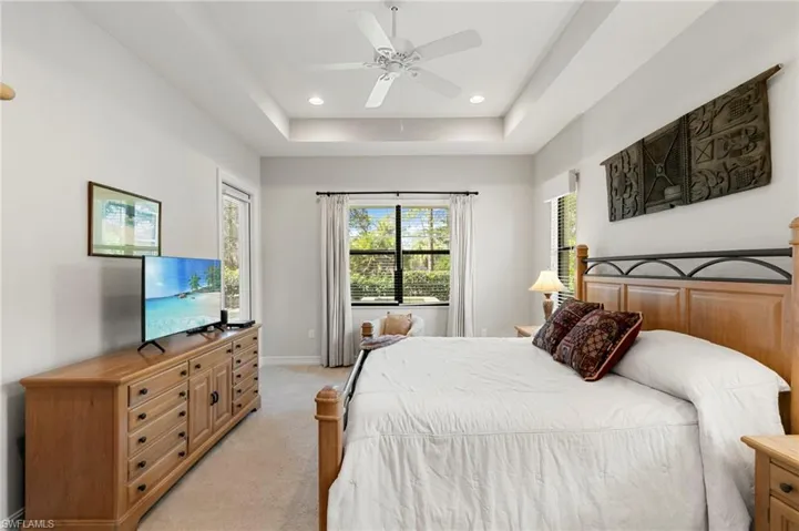 Bedroom with light carpet, a raised ceiling, a ceiling fan, and recessed lighting