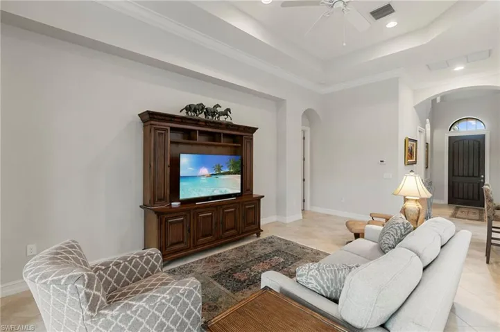 Living room with ornamental molding, light tile patterned floors, a ceiling fan, a tray ceiling, and recessed lighting