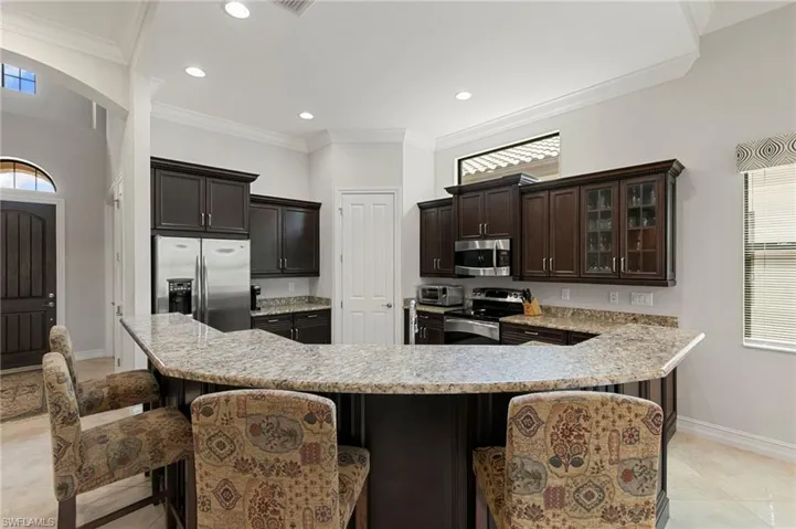 Kitchen featuring plenty of natural light, stainless steel appliances, a kitchen breakfast bar, dark wood finish cabinets, and ornamental molding