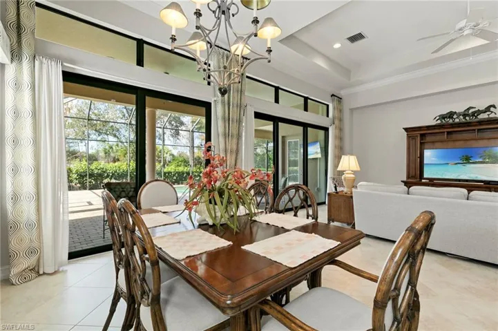 Dining area with crown molding, light tile patterned floors, ceiling fan, a chandelier, and a raised ceiling