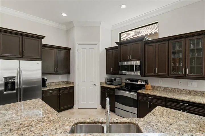 Kitchen featuring dark wood finish cabinets, stainless steel appliances, light stone countertops, glass fronted cabinets, and crown molding