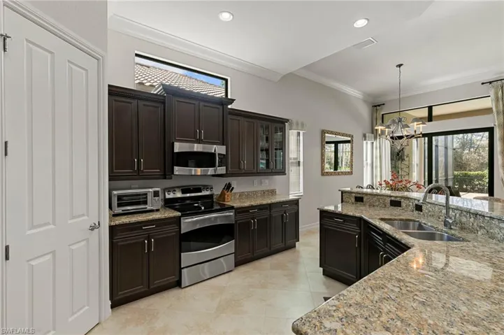 Kitchen featuring stainless steel appliances, glass insert cabinets, suspended lighting, light stone countertops, and ornamental molding