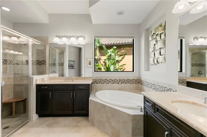 Bathroom featuring a stall shower, a garden tub, two vanities, and light tile patterned floors