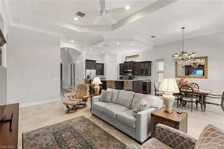 Living area with crown molding, arched walkways, ceiling fan, a chandelier, and a raised ceiling