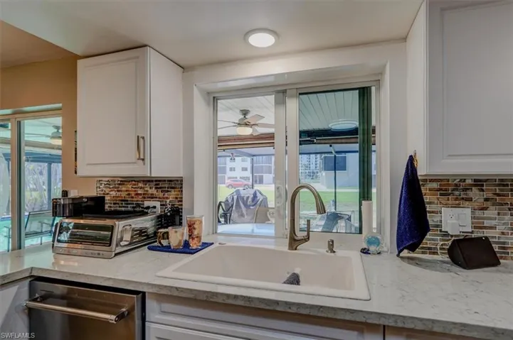 Kitchen with dishwasher, white cabinetry, sink, light stone counters, and ceiling fan