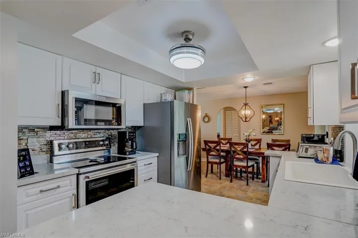 Kitchen featuring appliances with stainless steel finishes, tasteful backsplash, white cabinets, decorative light fixtures, and a raised ceiling