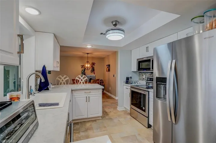 Kitchen featuring sink, stainless steel appliances, a tray ceiling, white cabinets, and decorative light fixtures