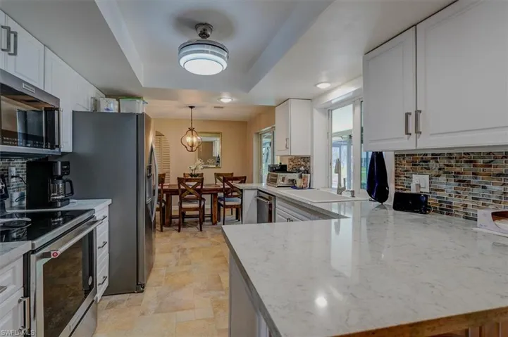 Kitchen with light stone counters, a tray ceiling, kitchen peninsula, stainless steel appliances, and white cabinets