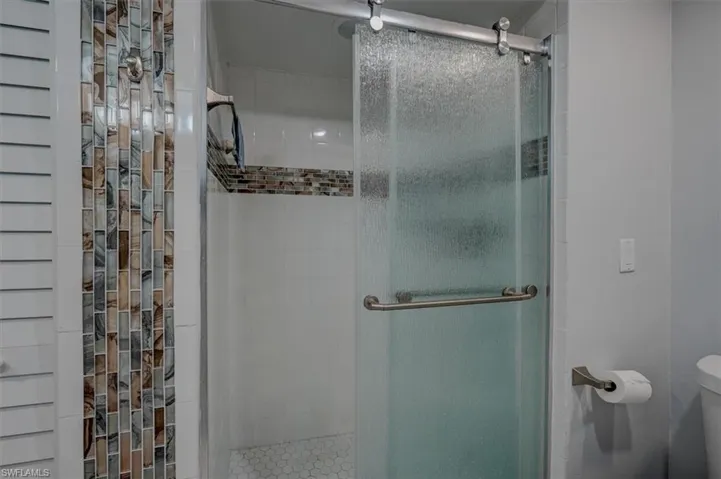 Bathroom featuring a shower with door and toilet